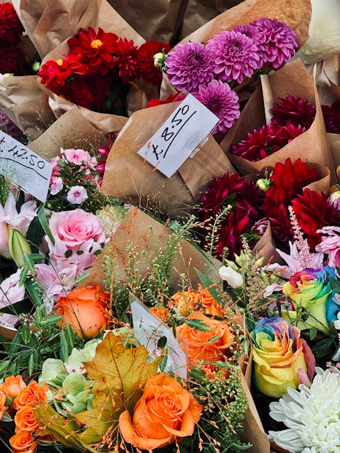 A vibrant assortment of freshly prepared flower bouquets featuring a variety of blooms such as red dahlias, purple chrysanthemums, pink roses, orange roses, and multicolored spray roses, arranged in b