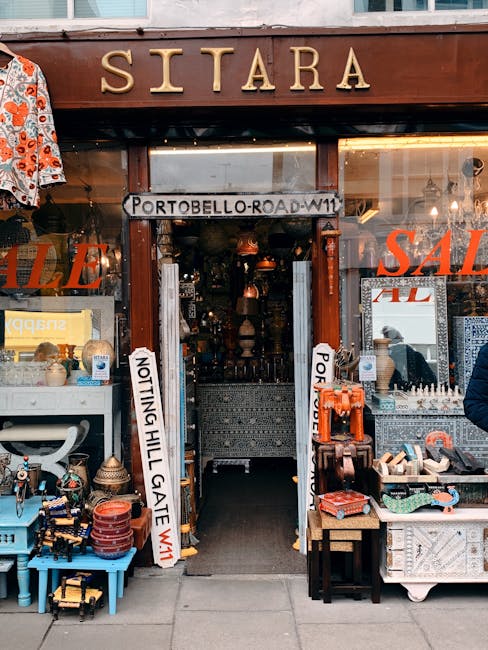 The entrance of Sitara, a shop on Portobello Road in Notting Hill, London, with a prominent brown wooden sign displaying the store's name. The shop window showcases various vintage and handcrafted ite