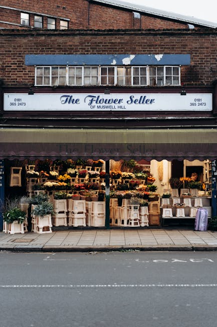 The storefront of The Flower Seller of Muswell Hill, showcasing an array of fresh floral arrangements and bouquets displayed on tables and shelves outside the shop. The flowers include various roses,