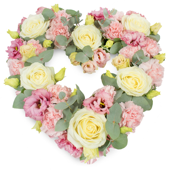 A beautifully composed heart-shaped floral wreath is presented on a clean white background, its soft colours and careful structure bringing to mind a peaceful corner of a London park in spring. The heart is luxurious and fully packed, ensuring a strong, continuous silhouette that symbolises unbroken love and cherished memory. Prominent throughout are large, creamy white to pale yellow roses, their velvety petals elegantly curled and layered, each bloom a focal point that suggests purity, gratitude, and an enduring bond. Between them, clusters of light, pastel pink carnations create a gently rippling texture, their frilled, multi-layered petals adding both volume and softness to the overall arrangement. Deeper pink to mauve lisianthus, with their subtly flared petals and occasional hints of darker centres, weave gracefully among the paler flowers, adding a more intense, emotional note that feels fitting for moments of farewell. Slender stems of silvery-green eucalyptus thread throughout the heart, their distinctive round leaves curving along the outline and filling in the background with a calm, muted green that offers balance and depth. Small yellow-green buds punctuate the design, like whispered reminders of youth, hope, and the ongoing rhythm of life in the city. The combination of colours-pink, cream, yellow, and cool green-creates a restful, harmonious impression, ideal for a funeral or memorial service held anywhere in London, from traditional churches to modern crematoria. Crafted with the eye of an experienced city florist, this wreath would sit beautifully beside the coffin or at the front of a ceremony, quietly reflecting the love and memories shared by family and friends.