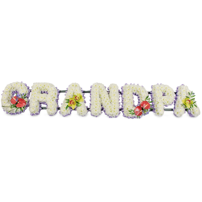 In this dignified funeral tribute, the word "GRANDPA" stretches across the frame in sturdy, block-style capital letters, created by a dense covering of white chrysanthemums. Each letter appears three-dimensional and solid, yet the tightly massed flowers lend a softness that gently tempers the bold shapes. The chrysanthemum heads are small and uniform, with layers of neat, rounded petals creating a padded, cushion-like effect that suggests comfort, peace, and a sense of gentle protection. The flowers are pristine white, catching the light in a way that gives the surface a subtle sheen without any glare. Around the base of every letter runs a narrow, pale lavender trim, likely ribbon or a similar material. This soft purple edging peeks out delicately beneath the blooms, outlining each form and introducing a calm, almost spiritual hint of colour. Dark green support bars run behind the letters, largely hidden from the front but adding a thin line of depth and structure so the tribute looks ready to rest on trestles in a chapel or crematorium. Four thoughtfully placed accent clusters bring moments of colour and emotion to the design. On the "G" and the letter "D" near the centre-right, glossy red anthuriums with their heart-shaped spathes and prominent yellow spadices emerge from lush green leaves and a few touches of smaller filler flowers, creating striking points of focus. The first and final "A" feature yellow-green orchids, their open, graceful blooms and fresh foliage offering a note of gentle brightness. This type of bespoke floral lettering, often prepared by London Flowers for families across the city, from quiet residential streets to busy central London venues, provides a meaningful way to spell out a relationship and honour a beloved grandfather at a funeral or celebration of life.