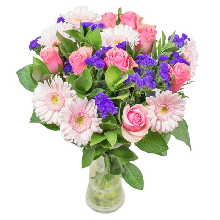 This elegantly arranged bouquet, set against a pristine white background in a flawless glass vase, showcases London's signature sense of style. Approximately seven to nine pink roses-some with tightly furled petals, others just about to blossom-form a classic spiral at the heart of the arrangement. These are beautifully accompanied by five to seven pale pink gerbera daisies, each large and radiant with subtly lighter centers, reminiscent of the blooms lining the city's Royal Parks. Clusters of rich purple statice or limonium are scattered throughout, offering striking visual contrast and a sense of textural diversity emblematic of London's own vibrant spirit. The base is enveloped in lush, deep green foliage, adding volume, freshness, and a layer of aromatic complexity. Visible stems and water within the slender vase highlight the bouquet's freshness-reflective of same-day delivery across Chelsea, Soho, and beyond. Ideal for birthdays, anniversaries, Mother's Day, or as a chic office accent, this arrangement weaves together feelings of joy, celebration, and affection, echoing the artistry and care of London's local florists.
